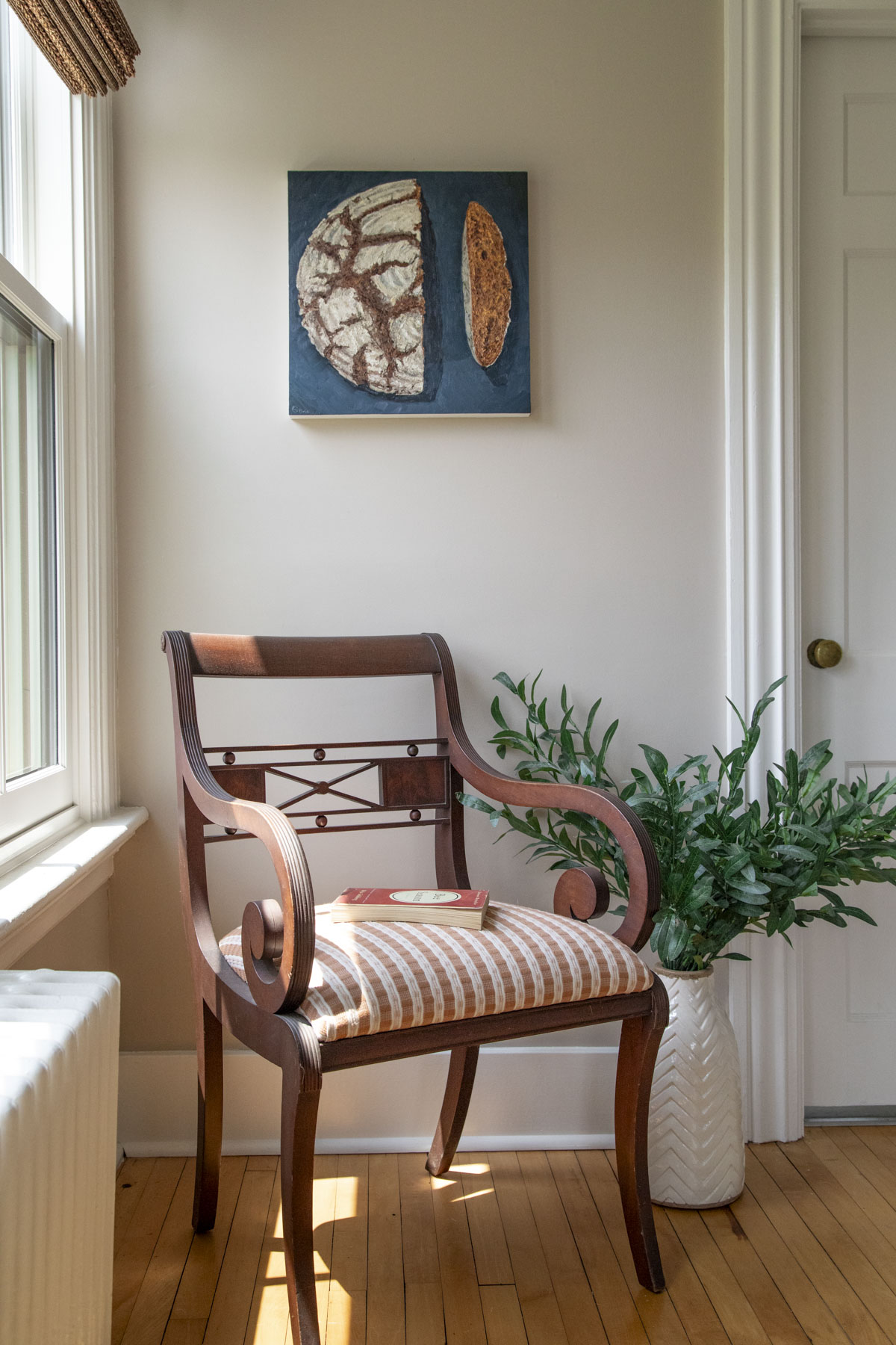 an antique chair with a pink cushion next to a taupe wall with a Mike Geno painting