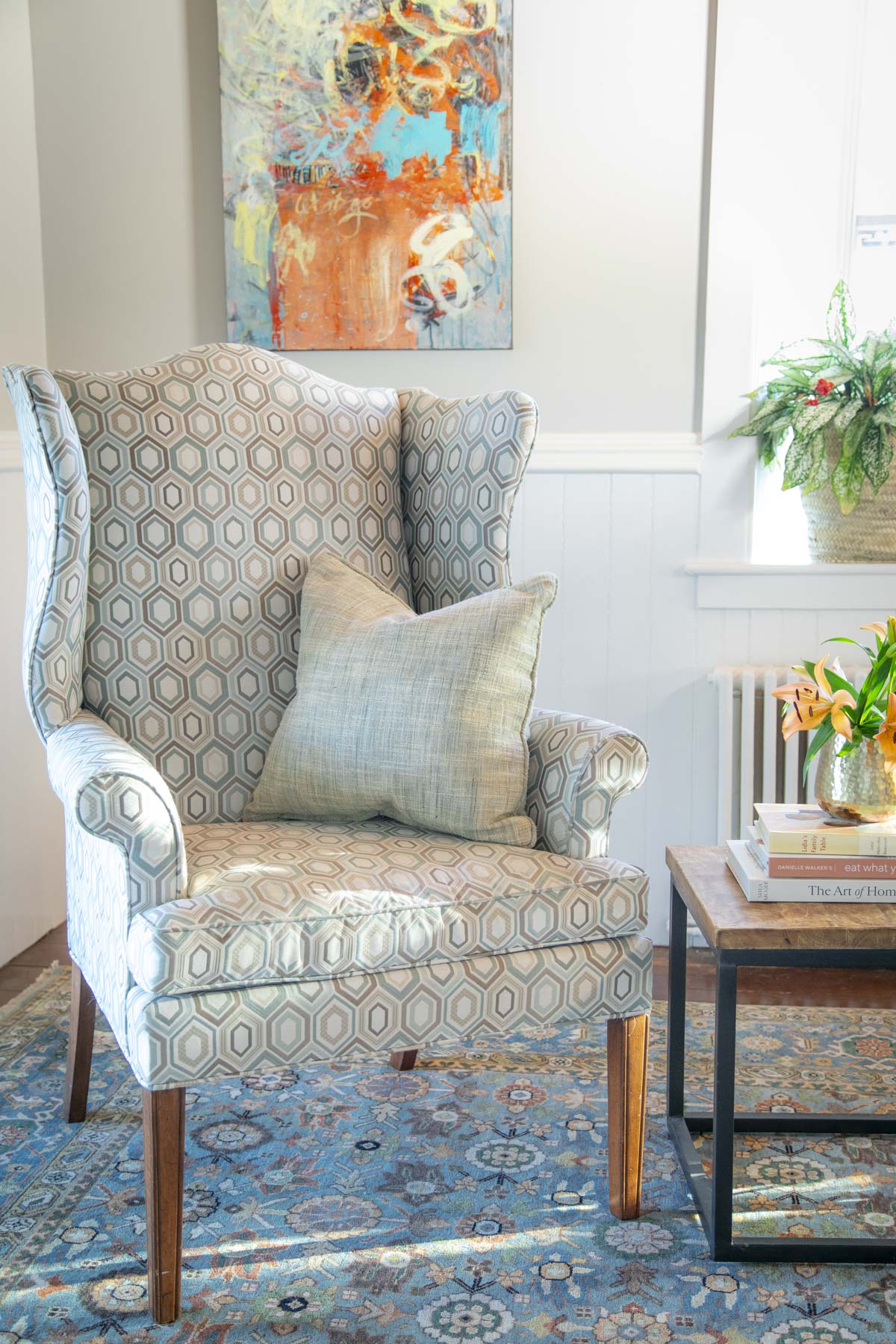 a wing chair with a modern art piece behind it and a blue rug